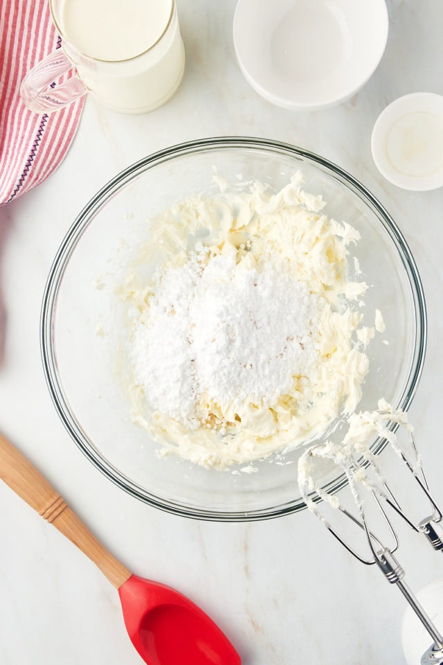 Overhead view of confectioners' sugar added to cream cheese in mixing bowl