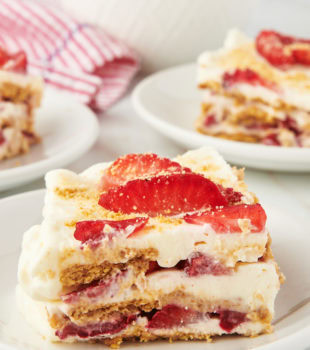 Slice of strawberry icebox cake on white plate with additional plates of cake in background