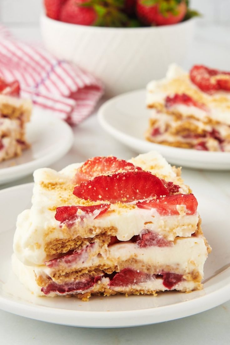 Slice of strawberry icebox cake on white plate with additional plates of cake in background