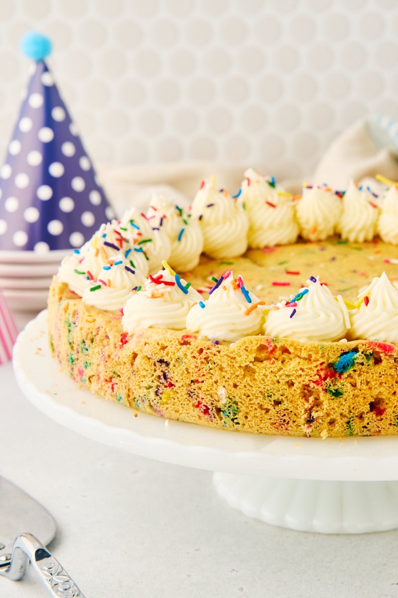 sugar cookie cake on a white cake stand with party hats in the background