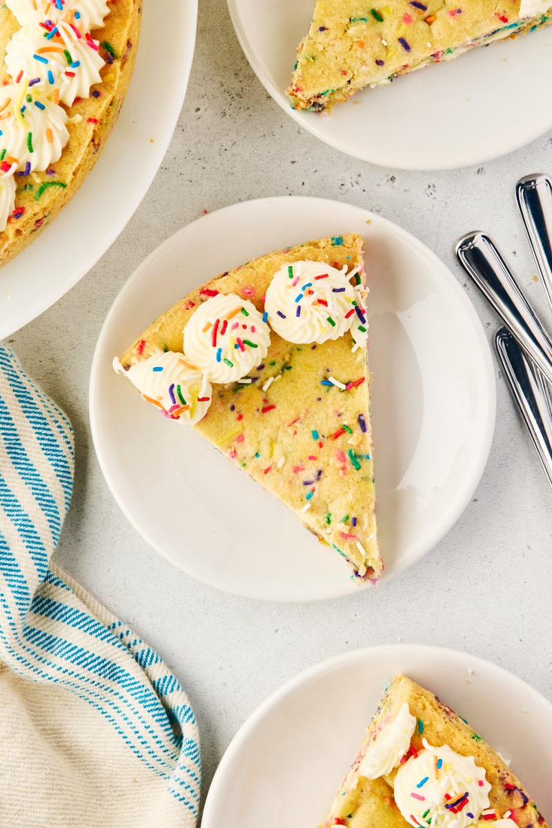 overhead view of a slice of sugar cookie cake on a white plate with more cookie surrounding