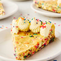 a slice of sugar cookie cake on a white plate with more servings in the background