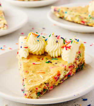 a slice of sugar cookie cake on a white plate with more servings in the background