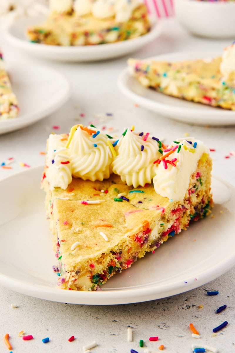 a slice of sugar cookie cake on a white plate with more servings in the background