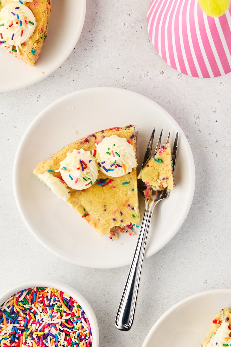 overhead view of a slice of sugar cookie cake on a white plate with a bite on a fork