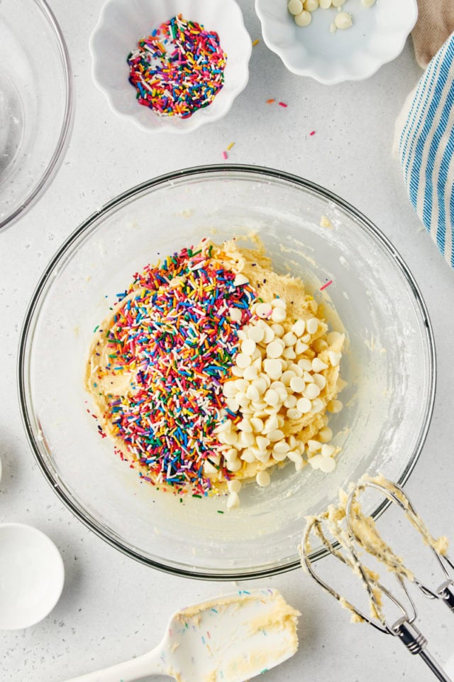 overhead view of white chocolate chips and rainbow sprinkles added to sugar cookie dough