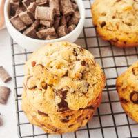 three thick chocolate chip cookies stacked on a wire cooling rack