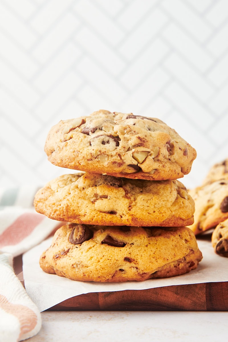 stack of three thick chocolate chip cookies on a wooden board