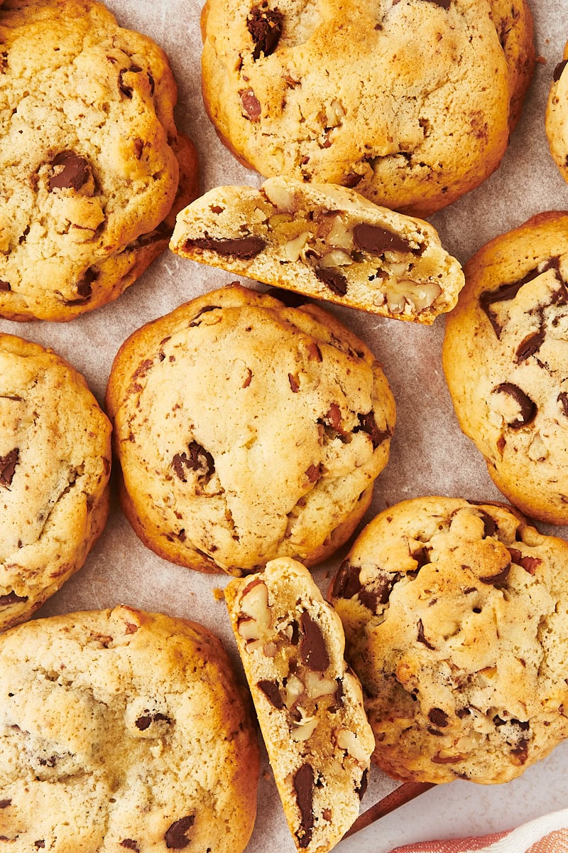 overhead view of thick chocolate chip cookies on a parchment paper, with some of the cookies broken in half to show the insides