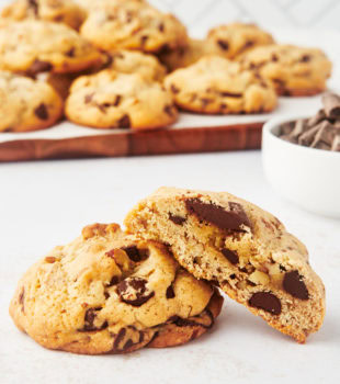 half of a thick chocolate chip cookie leaned against another cookie with a tray of cookies in the background