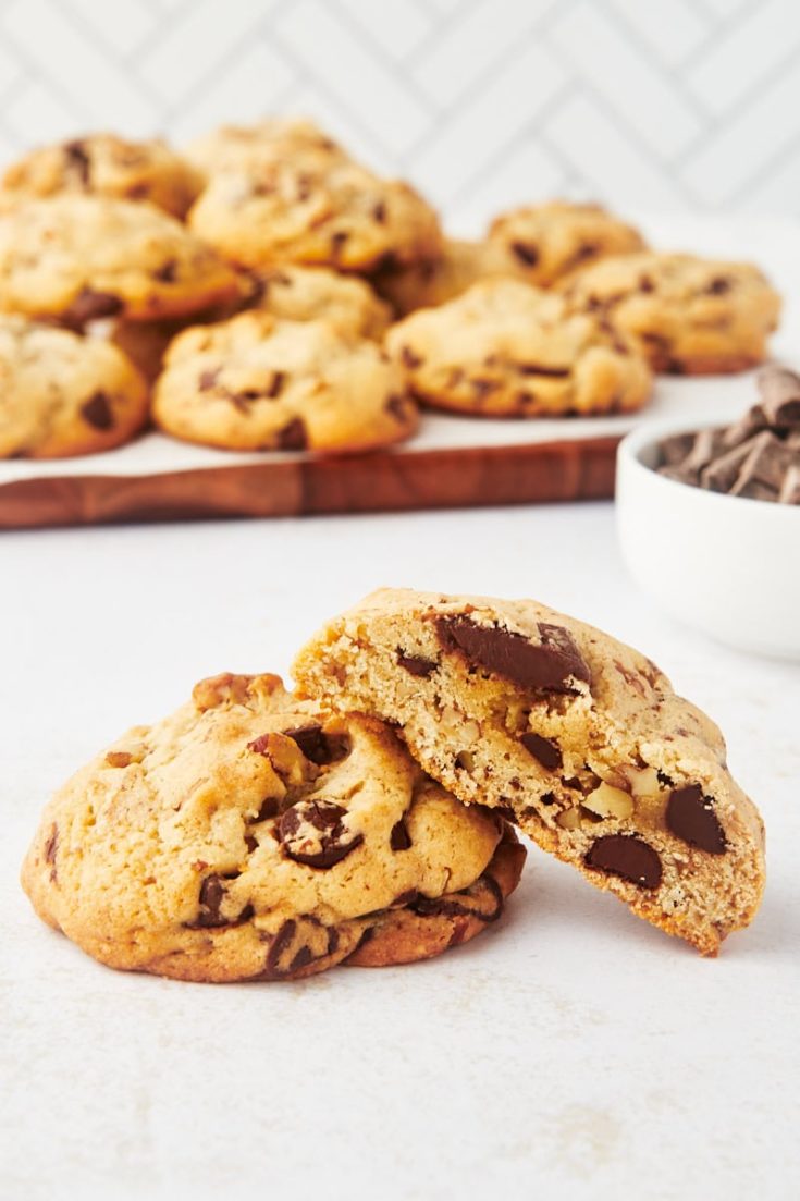 half of a thick chocolate chip cookie leaned against another cookie with a tray of cookies in the background