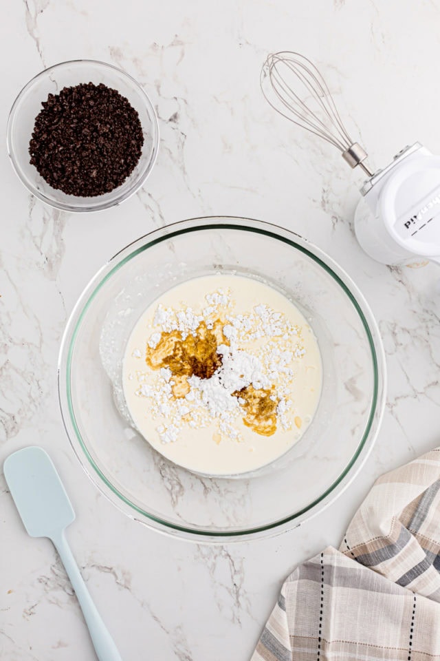 overhead view of heavy cream, confectioners' sugar, and vanilla in a glass mixing bowl