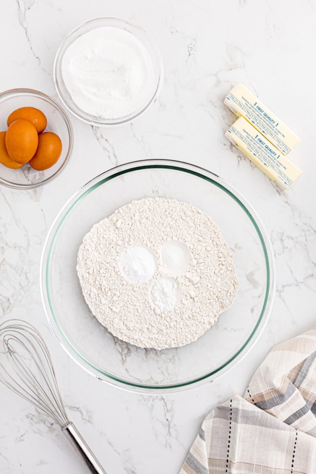 overhead view of flour, baking powder, baking soda, and salt in a glass mixing bowl