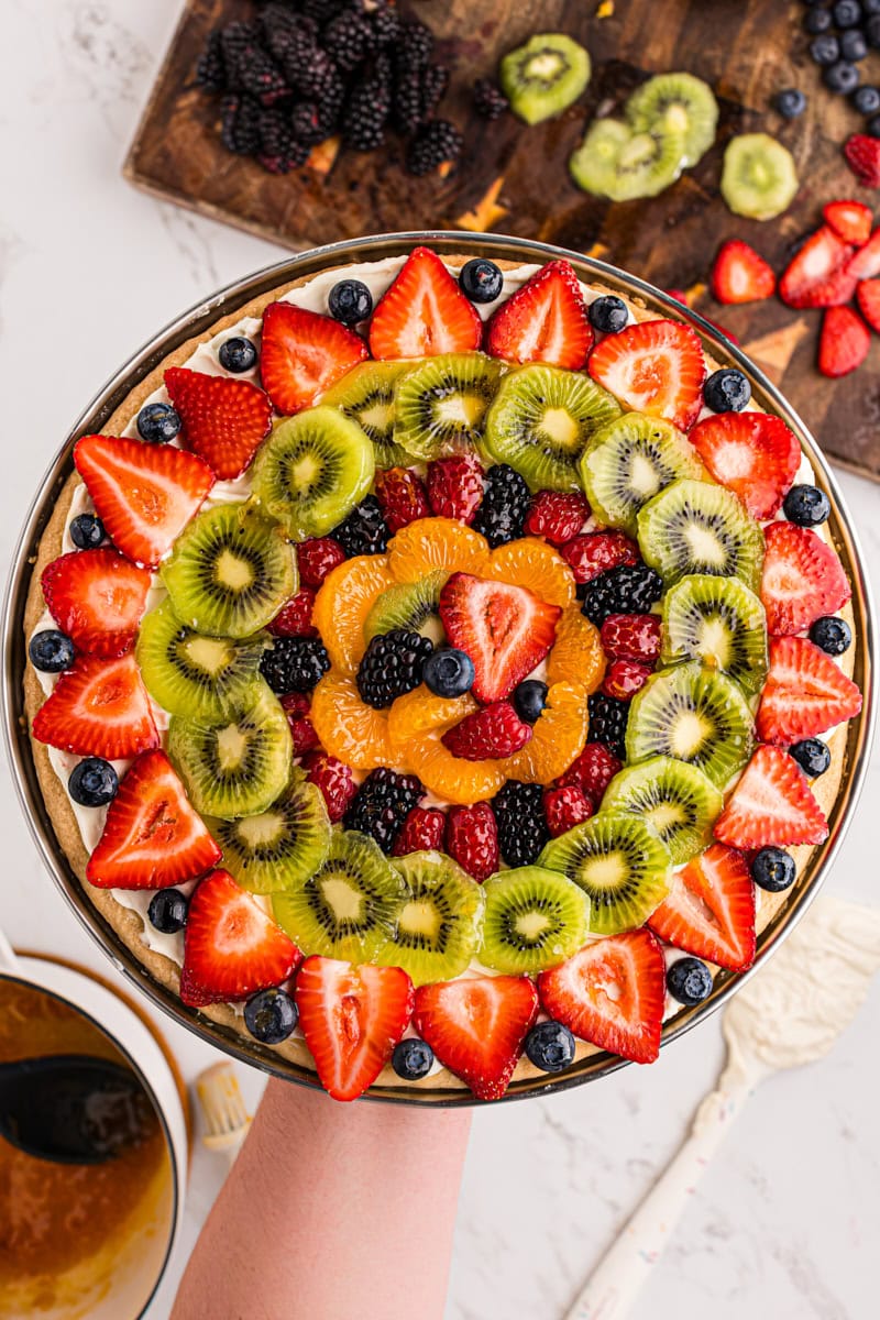 overhead view of fruit pizza being held above a marble countertop