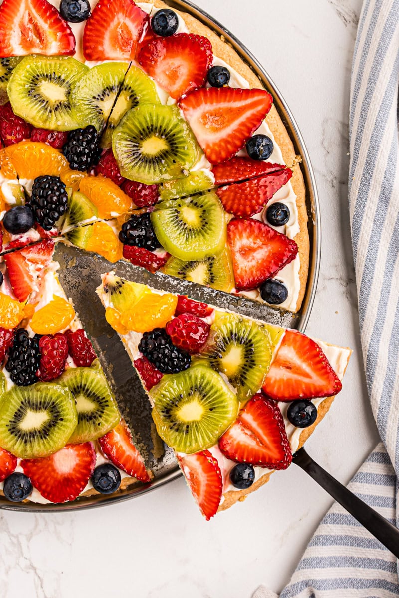 a slice of fruit pizza being pulled away from the remaining pizza