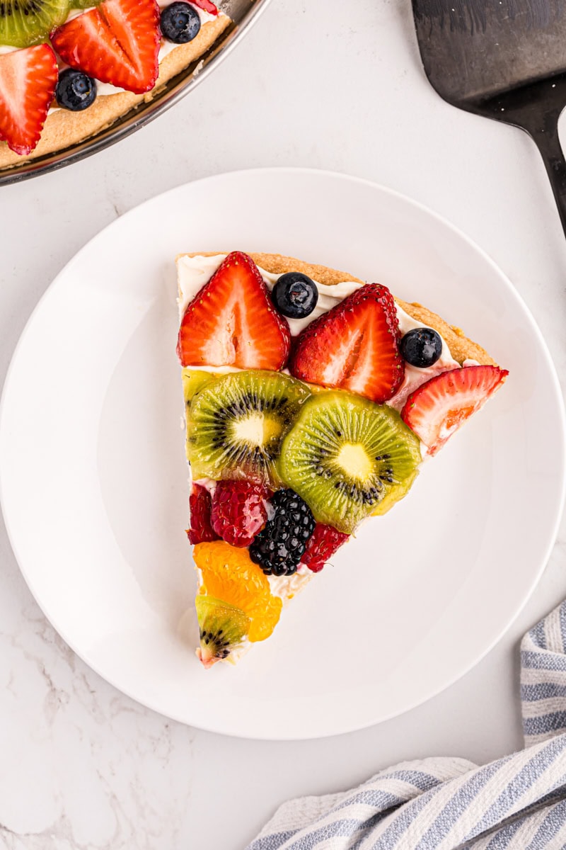 overhead view of a slice of fruit pizza on a white plate