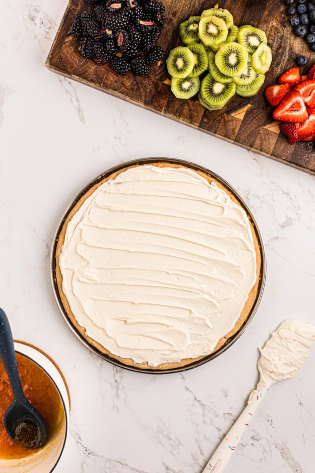 overhead view of cream cheese frosting spread on sugar cookie crust for fruit pizza