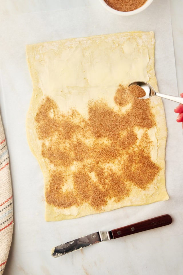 overhead view of cinnamon-sugar being sprinkled over buttered puff pastry