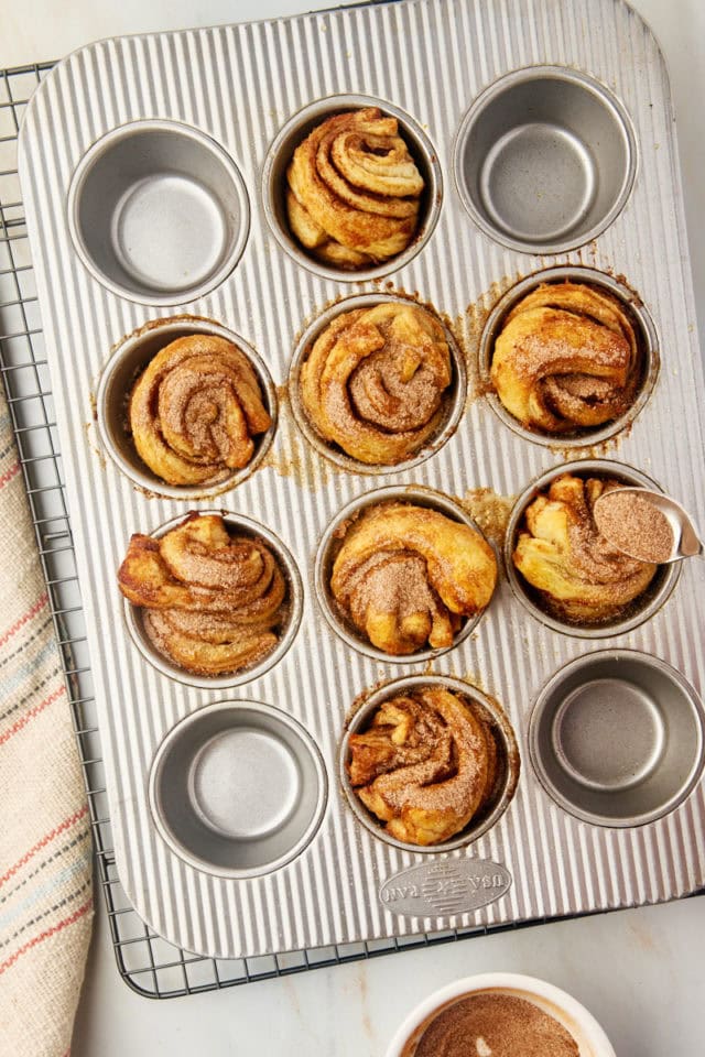 overhead view of freshly baked cruffins being sprinkled with cinnamon-sugar