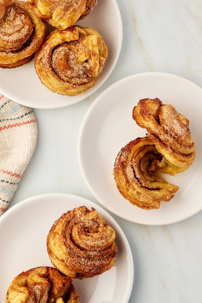 several cruffins on white plates, with one uncoiled to show the flaky layers