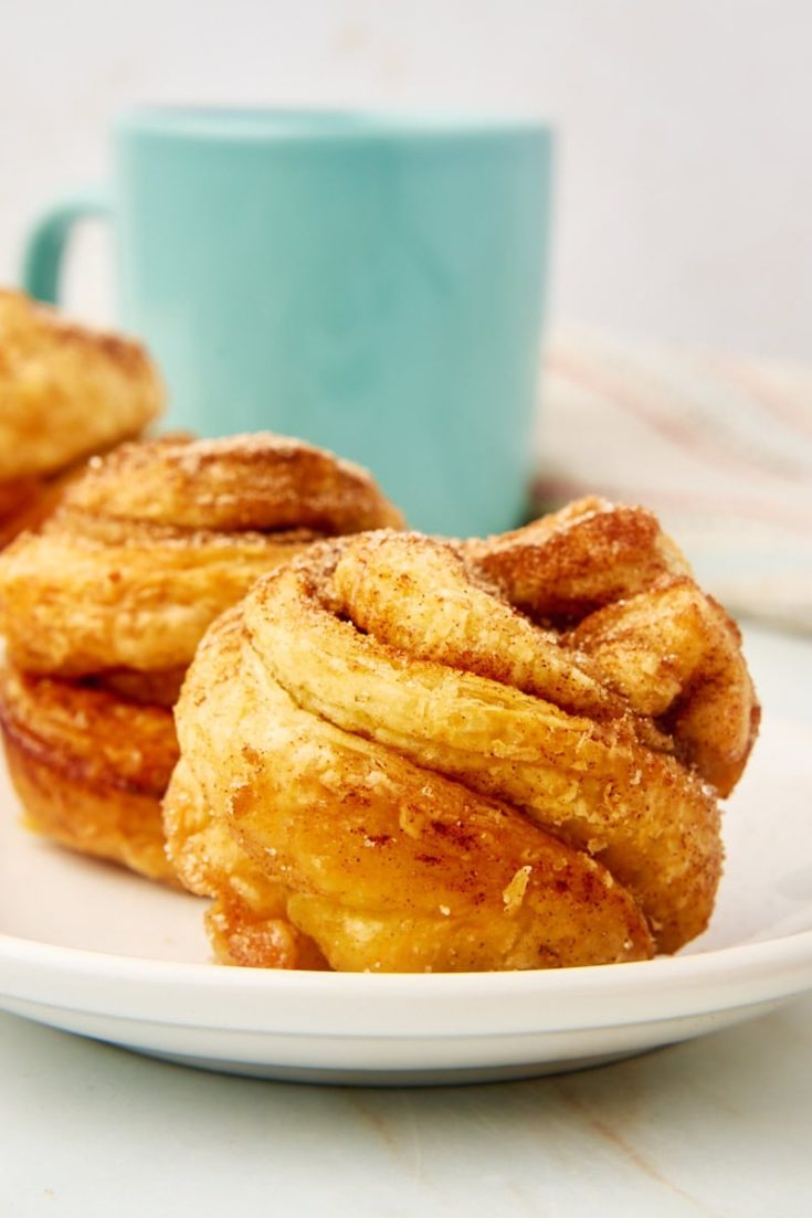 close-up view of a cruffin on a white plate with more cruffins and a coffee mug in the background