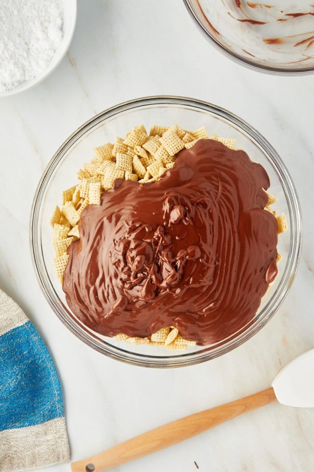 overhead view of chocolate-peanut butter mixture poured over rice Chex cereal in a glass mixing bowl