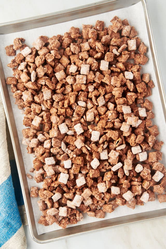 overhead view of muddy buddies spread on a lined baking sheet to cool