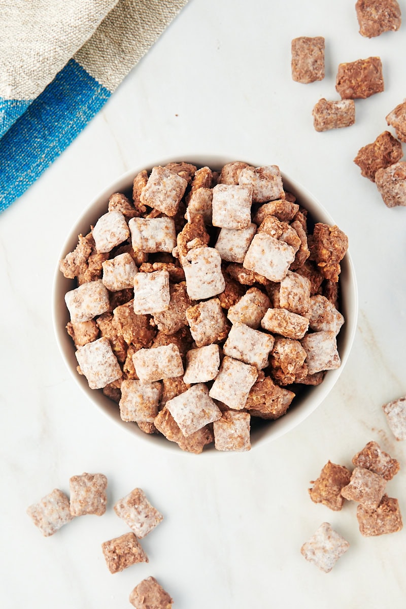 overhead view of muddy buddies in a white bowl with more scattered around the bowl