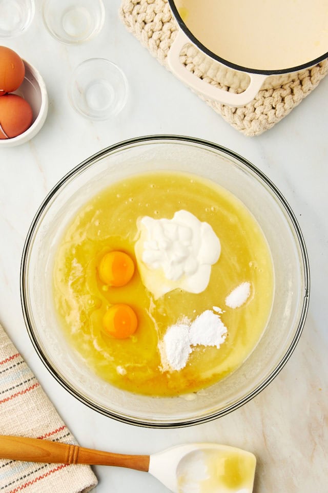 overhead view of eggs, sour cream, vanilla extract, almond extract, baking powder, baking soda, and salt added to flour mixture for white Texas sheet cake