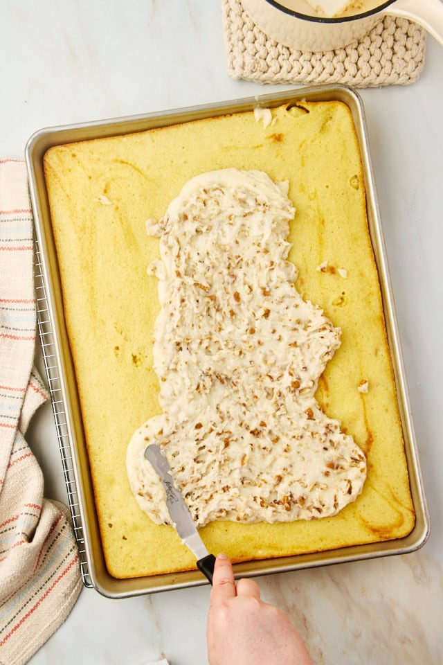 overhead view of frosting being spread on top of white Texas sheet cake