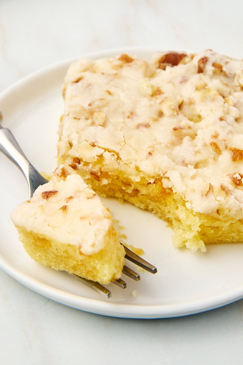 a slice of white Texas sheet cake on a white plate with a bite on a fork