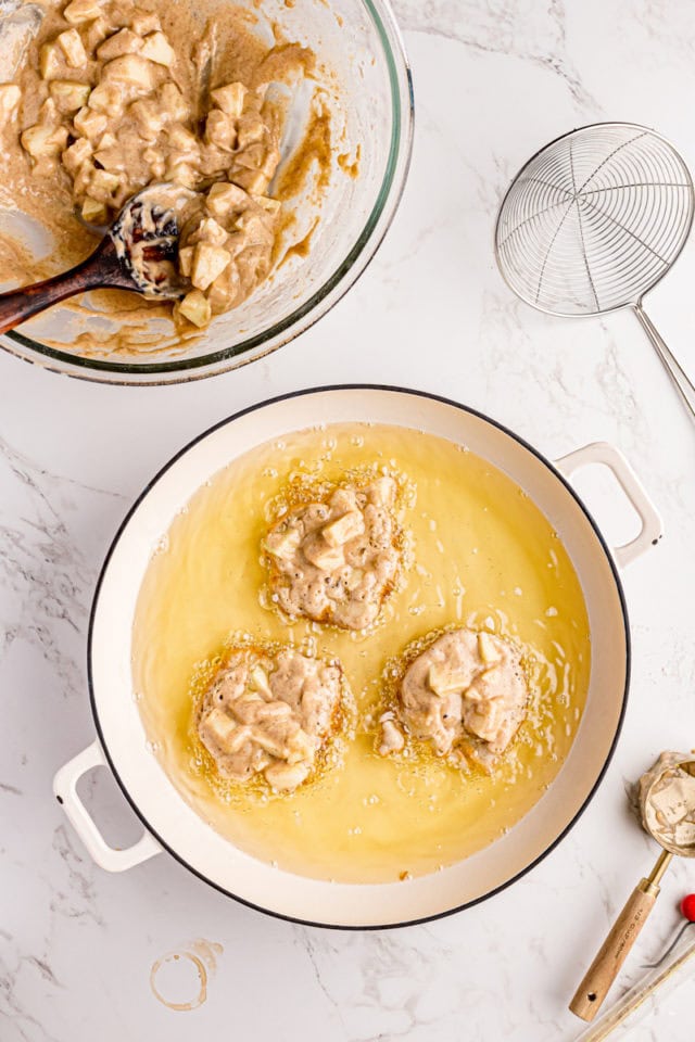 overhead view of apple fritters batter in a heavy pot filled with oil