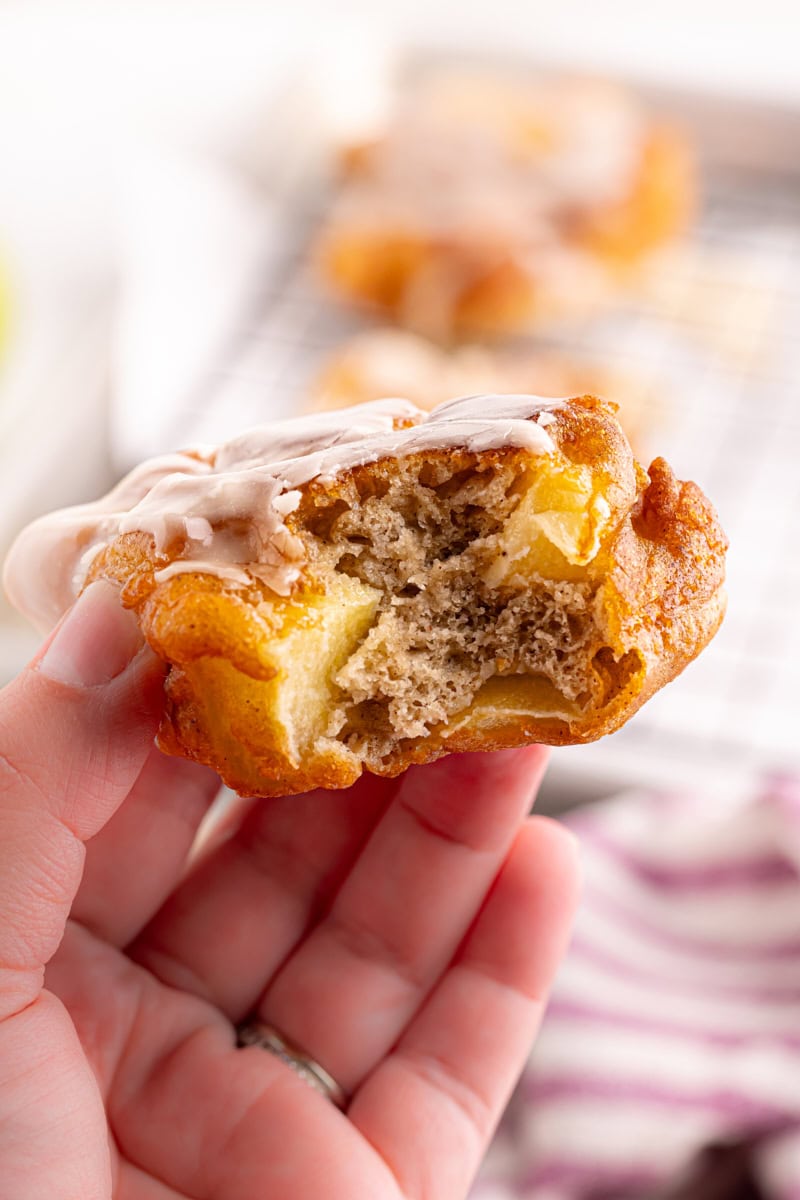 a hand holding an apple fritter with a bite missing to show the inner texture