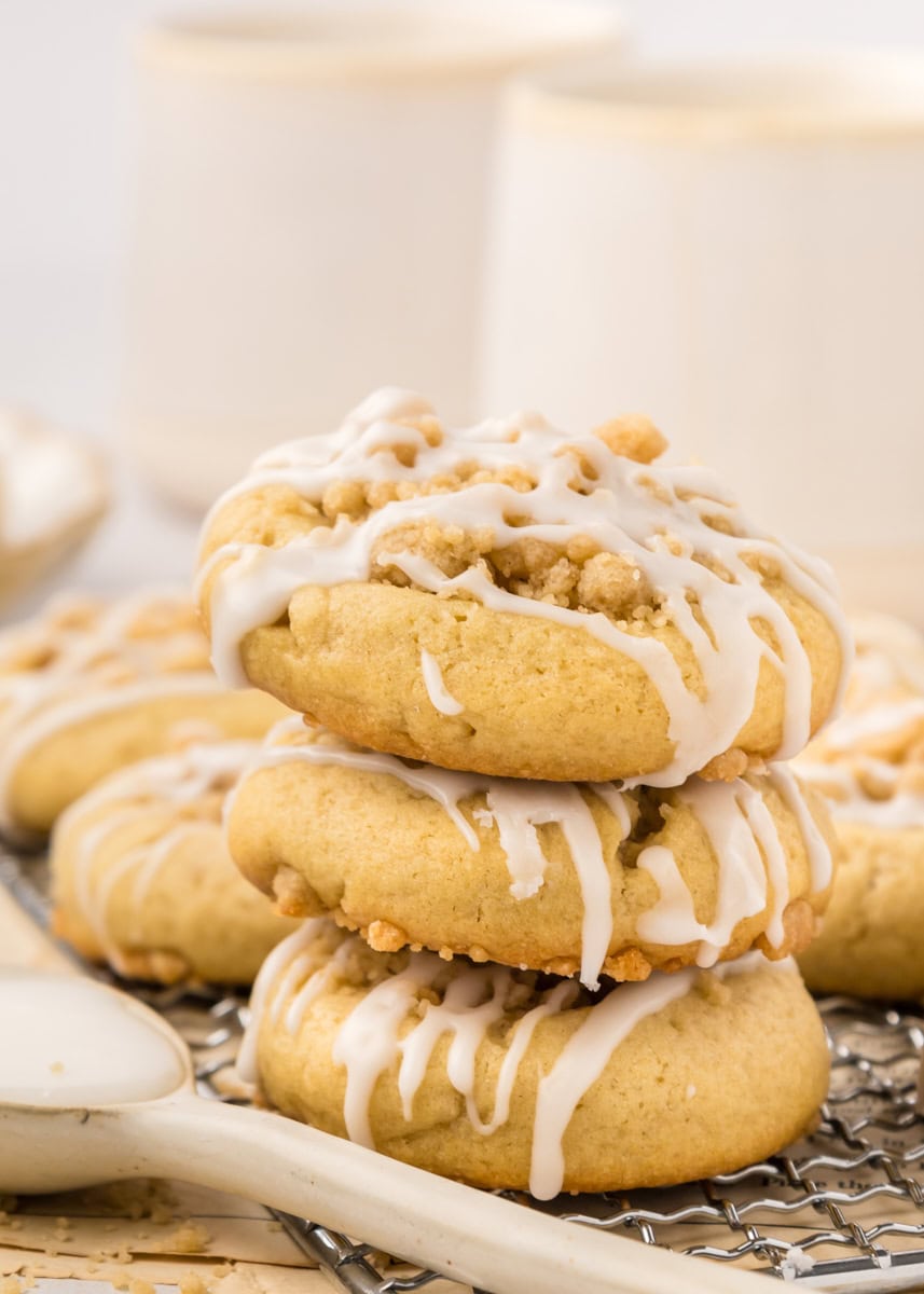 stack of three coffee cake cookies with more cookies and coffee mugs in the background