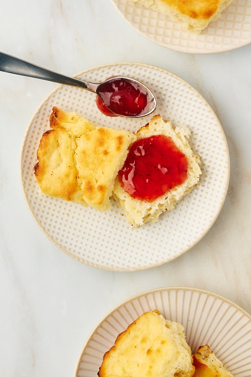 overhead view of strawberry jam spread on half of a butter swim biscuit