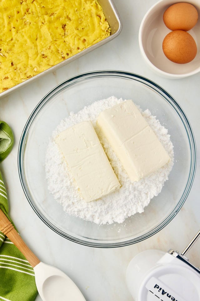 overhead view of cream cheese and confectioners' sugar in a glass mixing bowl