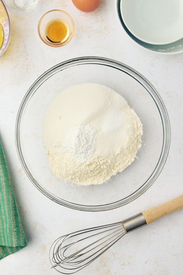 overhead view of flour, sugar, baking powder, and salt in a glass mixing bowl