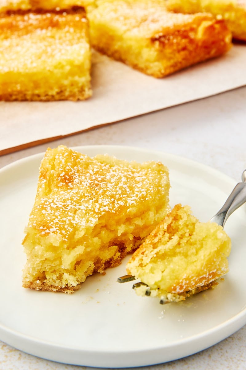 a slice of gooey butter cake on a white plate with a bite on a fork