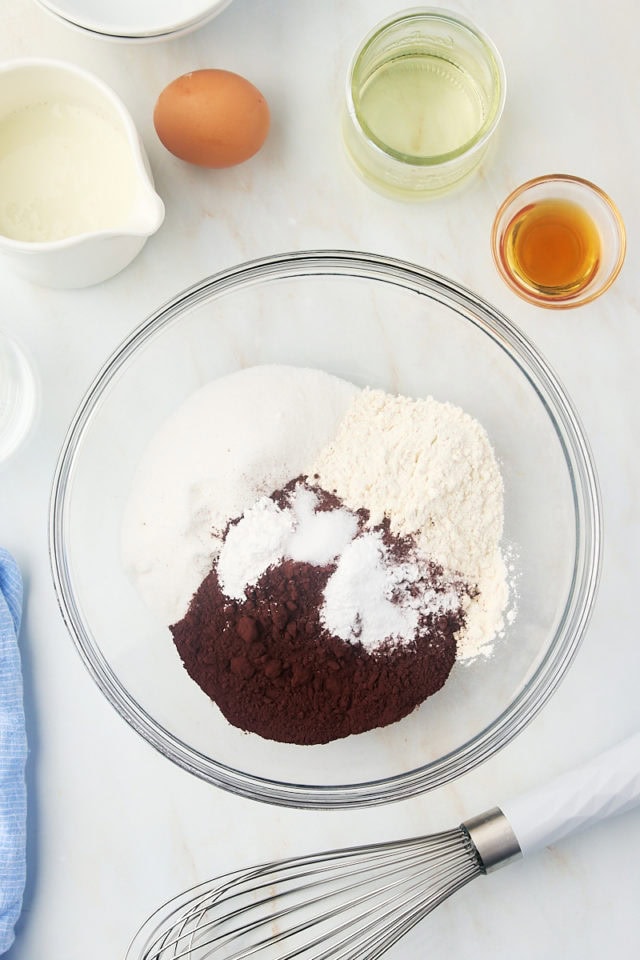 overhead view of sugar, flour, cocoa powder, baking powder, baking soda, and salt in a glass mixing bowl