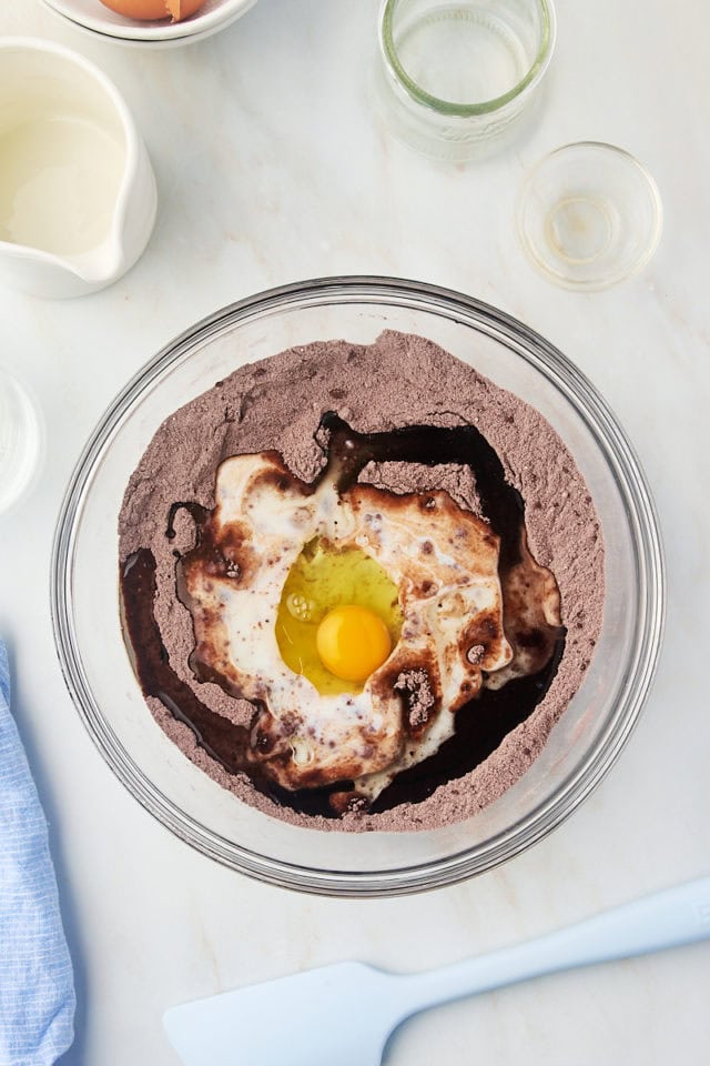 overhead view of egg, buttermilk, oil, and vanilla added to dry ingredients for one-bowl chocolate cake