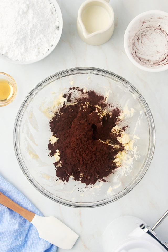 overhead view of cocoa powder added to creamed butter in a glass mixing bowl