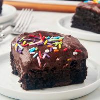 a slice of one-bowl chocolate cake on a white plate with more cake in the background