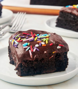 a slice of one-bowl chocolate cake on a white plate with more cake in the background