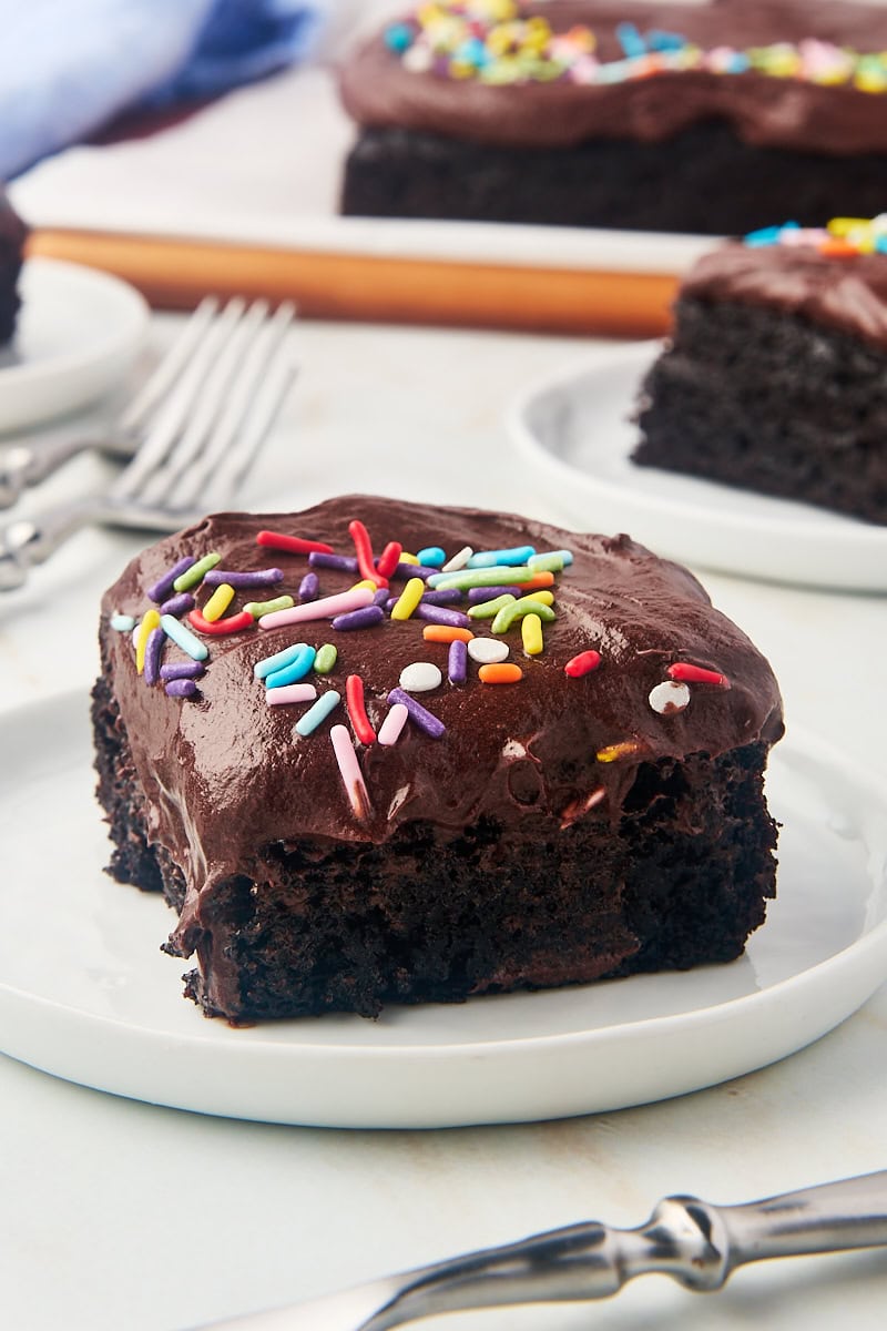 a slice of one-bowl chocolate cake on a white plate with more cake in the background