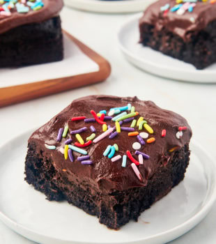 slice of one-bowl chocolate cake on a white plate with more cake in the background
