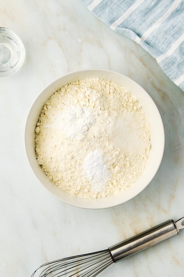 overhead view of flour, baking powder, baking soda, and salt in a white mixing bowl