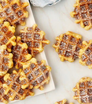 overhead view of waffle cookies on a white plate and scattered on a countertop