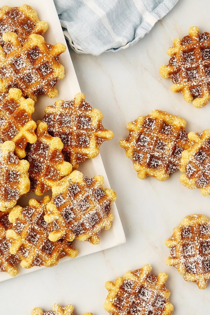 overhead view of waffle cookies on a white plate and scattered on a countertop