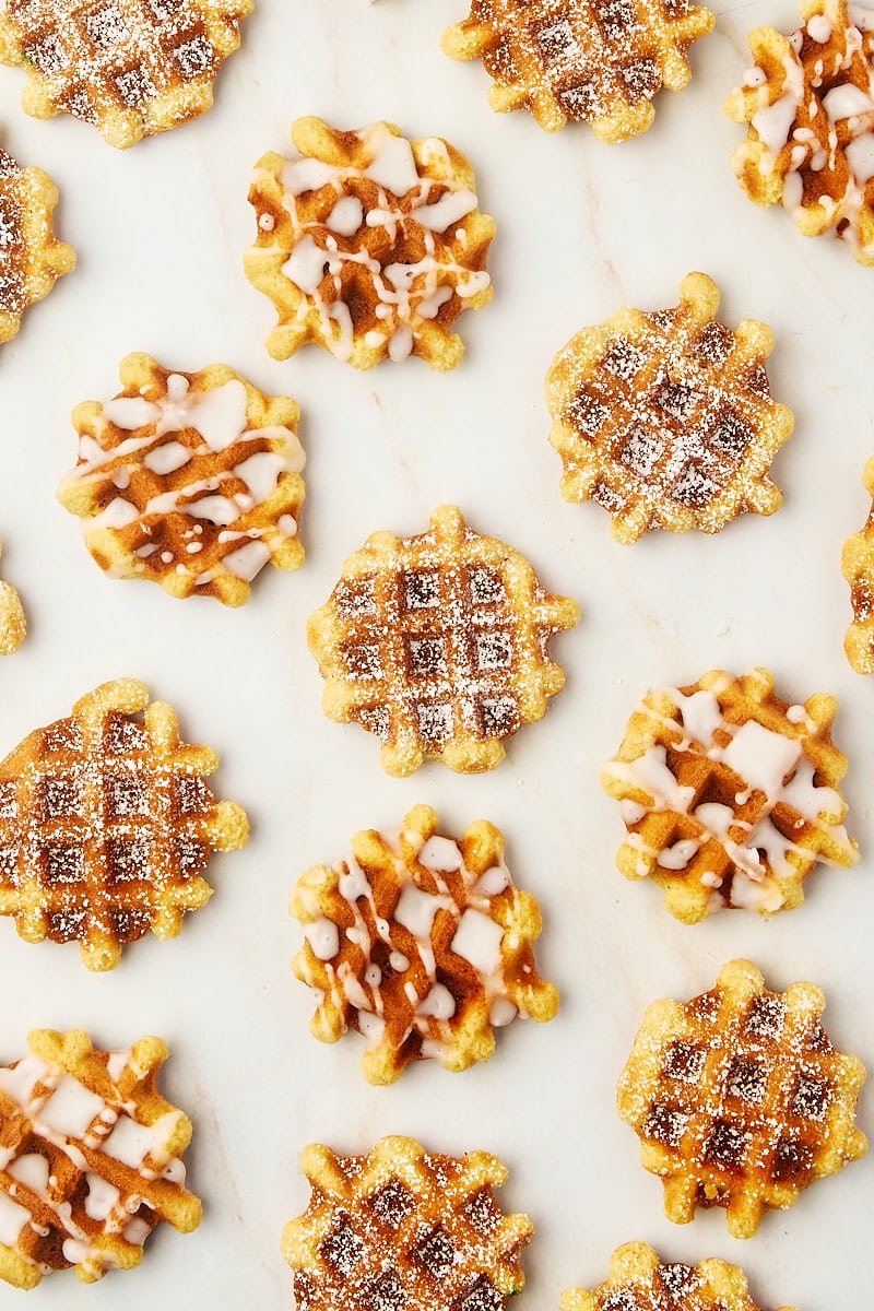 overhead view of waffle cookies, some topped with powdered sugar and some with a simple glaze