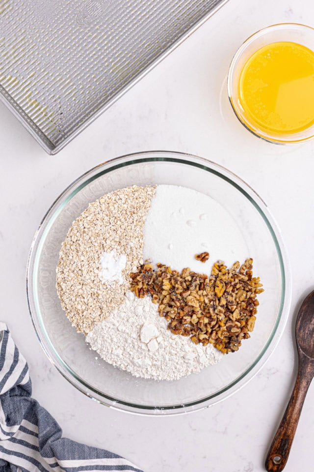 overhead view of flour, oats, sugar, nuts, and baking powder in a glass mixing bowl